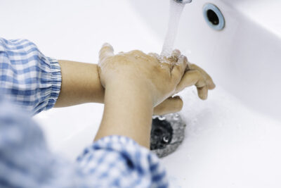 Child hands in school coat washing their hands under the tap
